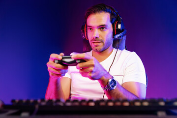 Smart gaming streamer concentrating gaming players trying to pass the level at mission completed with joystick control, talking others via mic on streaming live at neon lighting studio room. Surmise.