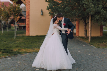 A bride and groom are dancing on a cobblestone path. The bride is wearing a white dress and the groom is wearing a blue suit