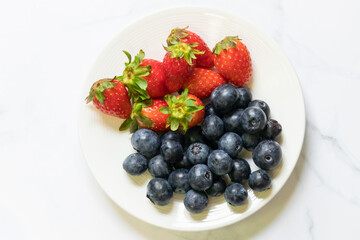Delicious and fresh strawberries and blueberries on a white plate, perfect for a healthy snack or dessert.