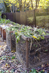 Compost bins for plant waste are set up in a garden to support eco-friendly recycling. Organic...
