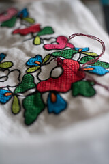 Close-up of colorful hand embroidery featuring vibrant flowers on white fabric, showcasing...