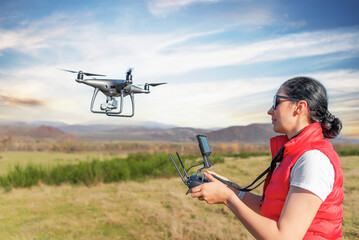 A young woman controls a drone with a remote control in her hands.