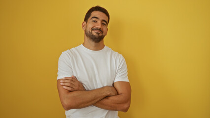 Confident young man with a beard stands with arms crossed against a vibrant yellow background, exuding handsome and attractive features, conveying a casual and isolated mood. © Krakenimages.com