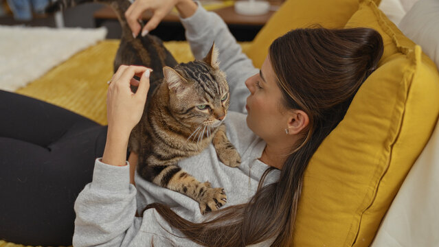A young hispanic woman relaxing on a bed with her playful cat in a cozy bedroom setting.