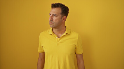 Hispanic man in yellow shirt standing over isolated yellow background, looking to the side, displaying a thoughtful expression, emphasizing the vibrant monochromatic theme.