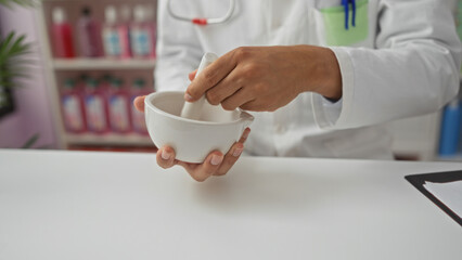 Male pharmacist grinding medicine in a white mortar inside a pharmacy.