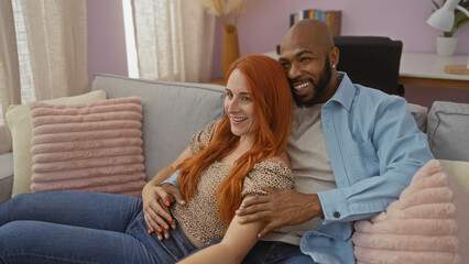 Interracial couple relaxing together on a cozy couch in a modern living room filled with light,...