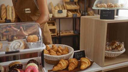 Young hispanic woman arranging pastries in a bakery with hands visible indoors featuring croissants...