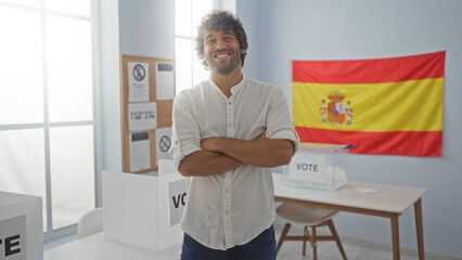 Young man smiling with arms crossed in a spanish electoral college with a spanish flag in the background