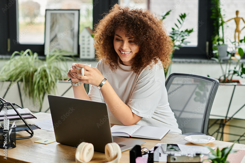 Wall mural A woman smiles with a coffee cup, concentrating on work at her colorful home office desk.