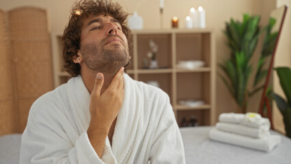 Fototapeta premium Man relaxing in a wellness spa wearing a bathrobe, surrounded by candles and plants, in a calm and serene setting focusing on self-care and pampering in a comfortable indoor environment.