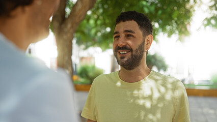 Two men having a friendly conversation in an urban park under the shade of trees, reflecting their bond, happiness, and outdoor enjoyment