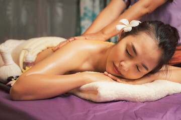 Spa therapist applying scrub salt and cream on young woman back at salon spa. Hands massaging female back with scrub.