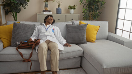 Tired female doctor with curly hair relaxes on a couch in a white lab coat in a cozy living room with a white isolated background