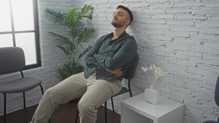 Handsome, young, hispanic man with a beard sitting and relaxing with arms crossed in a modern...