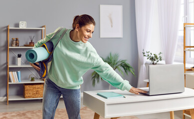 Young athlete woman with sports bag with equipment and sportswear, turning off laptop on desk,...