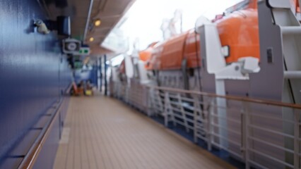 Blurred view of cruise deck with orange lifeboats and defocused bokeh lighting outdoors, featuring...