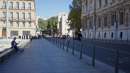 Naklejka premium Blurred scene of a man on a street in marseille with historic architecture and trees in the distance, creating a defocused, bokeh cityscape background.