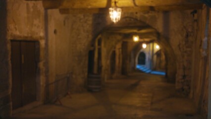 Blurred image of an old dark street at night with bokeh effect, showcasing defocused arches and stone walls in a mysterious, ancient urban setting.