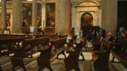 Blurred interior of a church with wooden pews, capturing defocused figures and religious art, creating a tranquil bokeh effect emphasizing the indoor setting.
