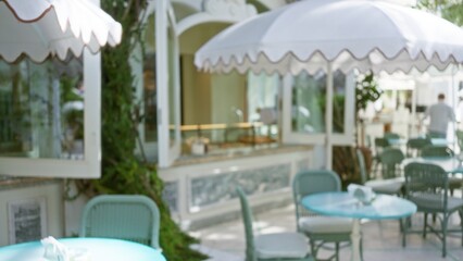 Outdoor dining area with blurred background of elegant luxury restaurant terrace featuring defocused furniture and bokeh effect with subtle greenery and ambient lighting.