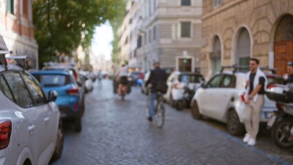 Blurry city street scene in rome, italy with bokeh effect, featuring people, cars parked, and cobblestone road in the old town, creating a nostalgic urban atmosphere.