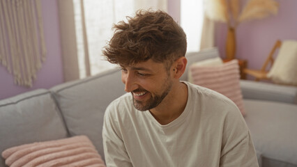 Young man smiling indoors in a cozy living room setting with pastel decor and plush cushions, showcasing a relaxed home atmosphere