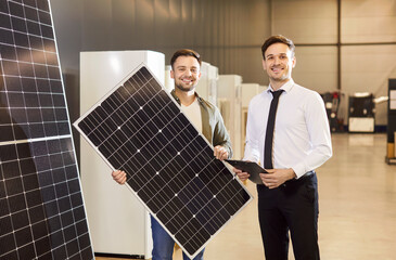 Portrait of a happy male consultant and customer holding a solar panel in a hardware shop....