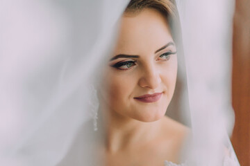 A woman with a veil over her face is smiling. She is wearing a white dress and has red lipstick