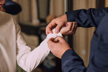 Two men are getting dressed up, one of them is putting a cuff on the other. The man putting the...