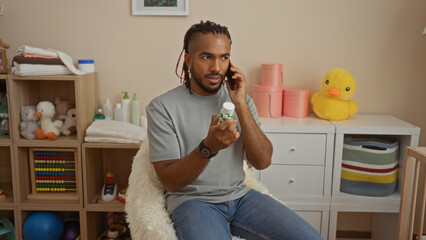 Man sitting indoors, talking on phone, holding medicine bottle, surrounded by toys, shelves, stuffed animals, and decorations, conveying casual, home, living room atmosphere.