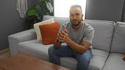 Young man with braids sitting on a sofa in a cozy living room with pillows and plants, exuding a...