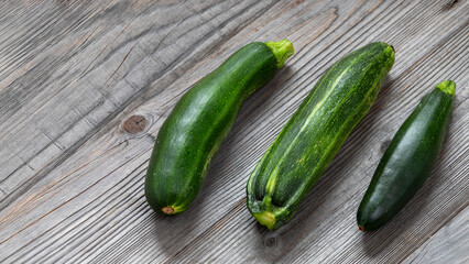 Three freshly harvested zucchini on a rustic wooden background with space for text.