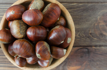 Edible raw chestnuts in a wooden bowl on the table. The concept of autumn food. Street food. Selective focus. Horizontal orientation. Top view. Copy space