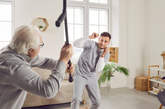 Aggressive old male patient attacking young nurse man with walking stick, expressing anger. Senior nursing problem, health care of elderly people job difficulty in mental emotional dangerous situation