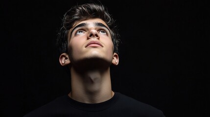 Obraz premium Serious Young Man Looking Upward with Thoughtful Gesture Against Dark Background Capturing Contemplative Mood and Reflective Expression in Studio Lighting