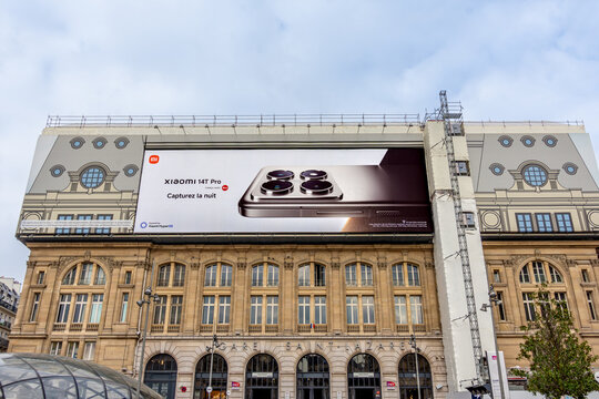 Paris, France - 14 novembre 2024: Affiche publicitaire g&eacute;ante pour le smartphone Xiaomi 14T Pro couvrant les &eacute;chafaudages des travaux de restauration sur la fa&ccedil;ade de la gare Saint Lazare
