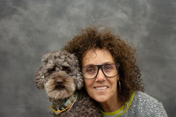 Portrait of a woman owner with his poodle dog with similar eyes and curly hair looking at camera