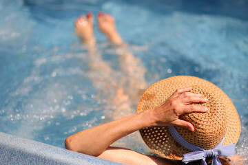 woman with hand on straw hat on head sitting inside the tub with massaging and relaxing bubbles