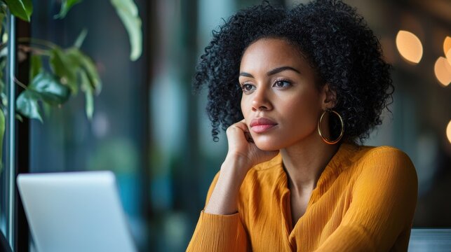 Young businesswoman thinking deeply while sitting in front of an open laptop, reflecting on work-related emails.