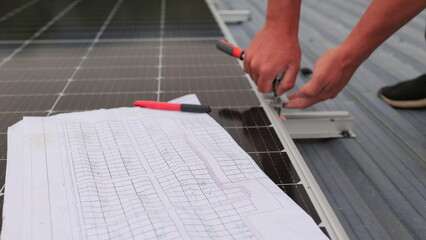 Close up of worker installing and working on maintenance of photovoltaic panel system installed. In the foreground is a diagram of the installation of solar panels. Solar panels on roof top