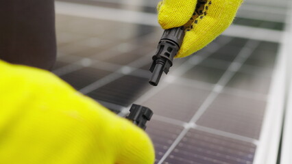Close up of connecting electric cable to solar panels. Connection and installation of solar panels. Connection to the solar energy network. An electrician in gloves connects the cable.