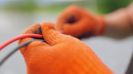 An electrician worker holds a red and black high-voltage electric cable, checks the quality of the cables. Connecting electrical cables. Close up of male hands in protective gloves holding cable.