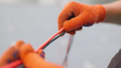 An electrician worker holds a red and black high-voltage electric cable, checks the quality of the cables. Connecting electrical cables. Close up of male hands in protective gloves holding cable.
