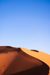 Desert landscape of sand dunes with traces of wheeled vehicles, people and camels at sunset. Erg Chebbi. Merzouga. Sahara desert. Morocco. Africa.