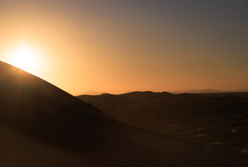Backlit sand dunes desert landscape at sunset, with tourists on the horizon.  Erg Chebbi. Merzouga. Sahara. Morocco. Africa.