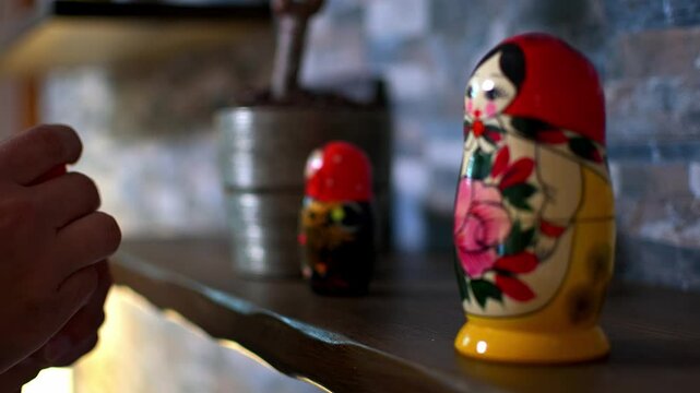 A man's hands are opening and placing a  Matryoshka doll placed on a wooden shelf of a home. Close up video with selective focus and shallow depth of field.