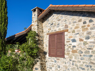 natural stone house wall with roof, chimney and shuttered wooden window, Cyprus