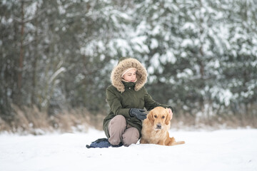 Beautiful young girl walking with a purebred retriever near a snowy forest in winter.