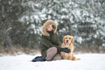 Beautiful young girl walking with a purebred retriever near a snowy forest in winter.